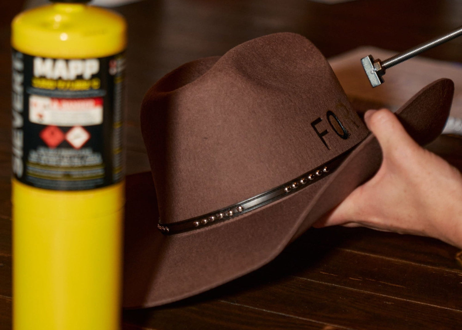 Brown cowboy hat on a table with a yellow MAPP gas canister and tools in the foreground.
